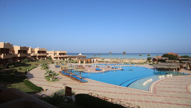 Ein Poolbereich eines Resorts mit mehreren Liegestühlen, einem großen Schwimmbecken und Blick auf den Ozean.
