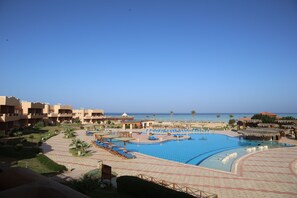 A resort pool area with multiple lounge chairs, a large swimming pool, and a view of the ocean. - Laguna Beach Marsa Resort (Marsa Alam)