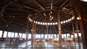 Ein geräumiger Saal mit hohen Holzbalken und einer Rundkuppel, ausgestattet mit Tischen und Stühlen für das Esserlebnis.