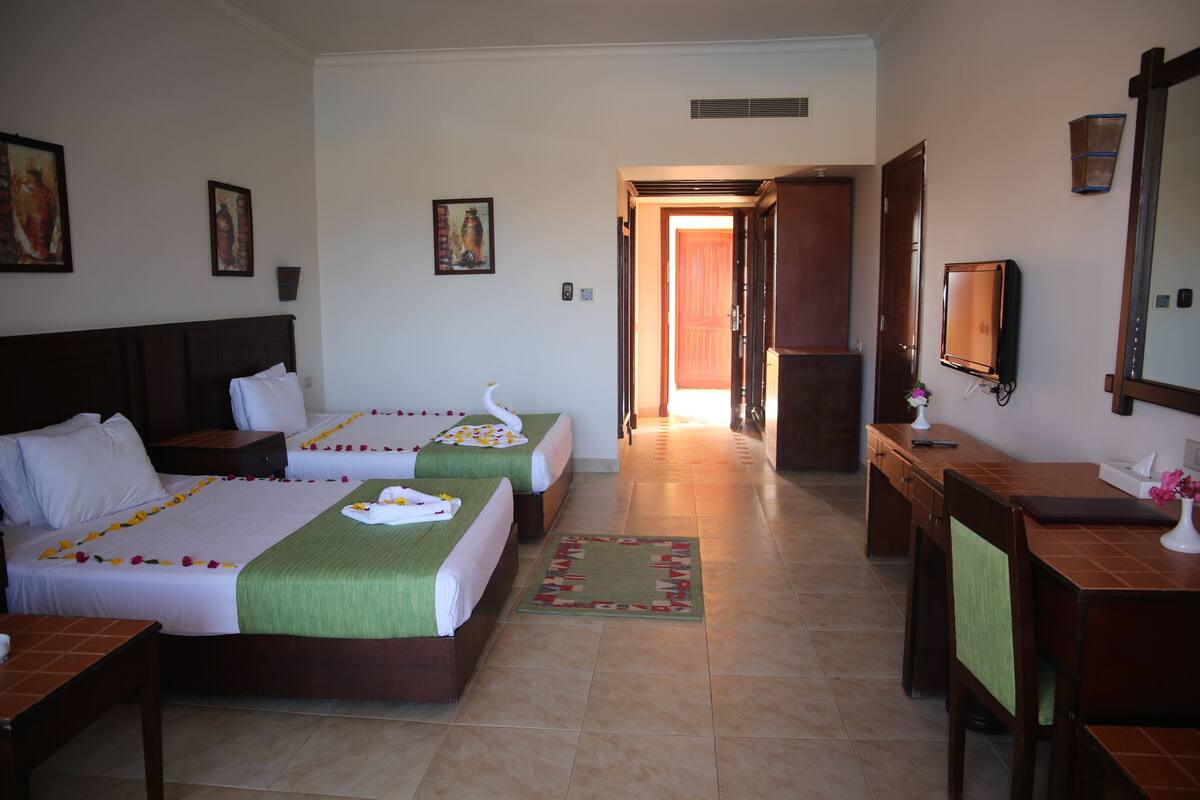 A hotel room with two beds, a desk, a chair, and a bathroom visible through an open door.