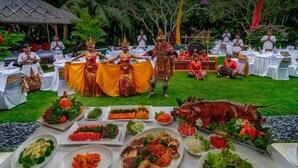Ceremonia tradicional con artistas en trajes elaborados, una mesa decorada con diversos platillos y un lechón asado como pieza central.