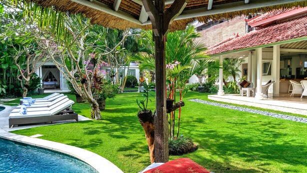 Un área junto a la piscina con una silla de descanso, un cojín rojo y una estructura de techo de paja.