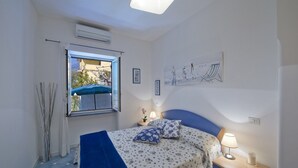 A bedroom with a bed, a nightstand, a lamp, a window with a view, and a ceiling fan. - Casa Agata (Praiano)