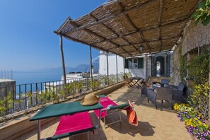 Una terraza con una mesa, sillas, un sombrero y vistas al mar.
