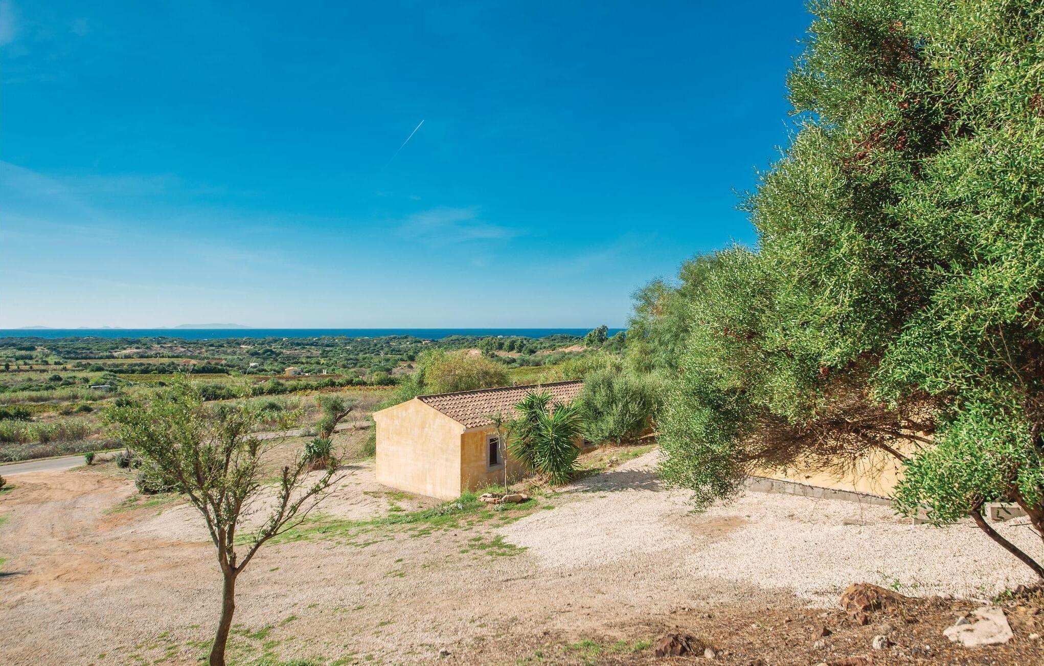 A small building with a tiled roof, surrounded by dry grass and sparse vegetation, overlooking a hilly landscape with a clear blue sky.