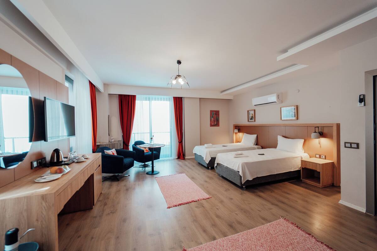 Une chambre d’hôtel moderne avec un bureau en bois, deux lits, une télévision et un coin repas.