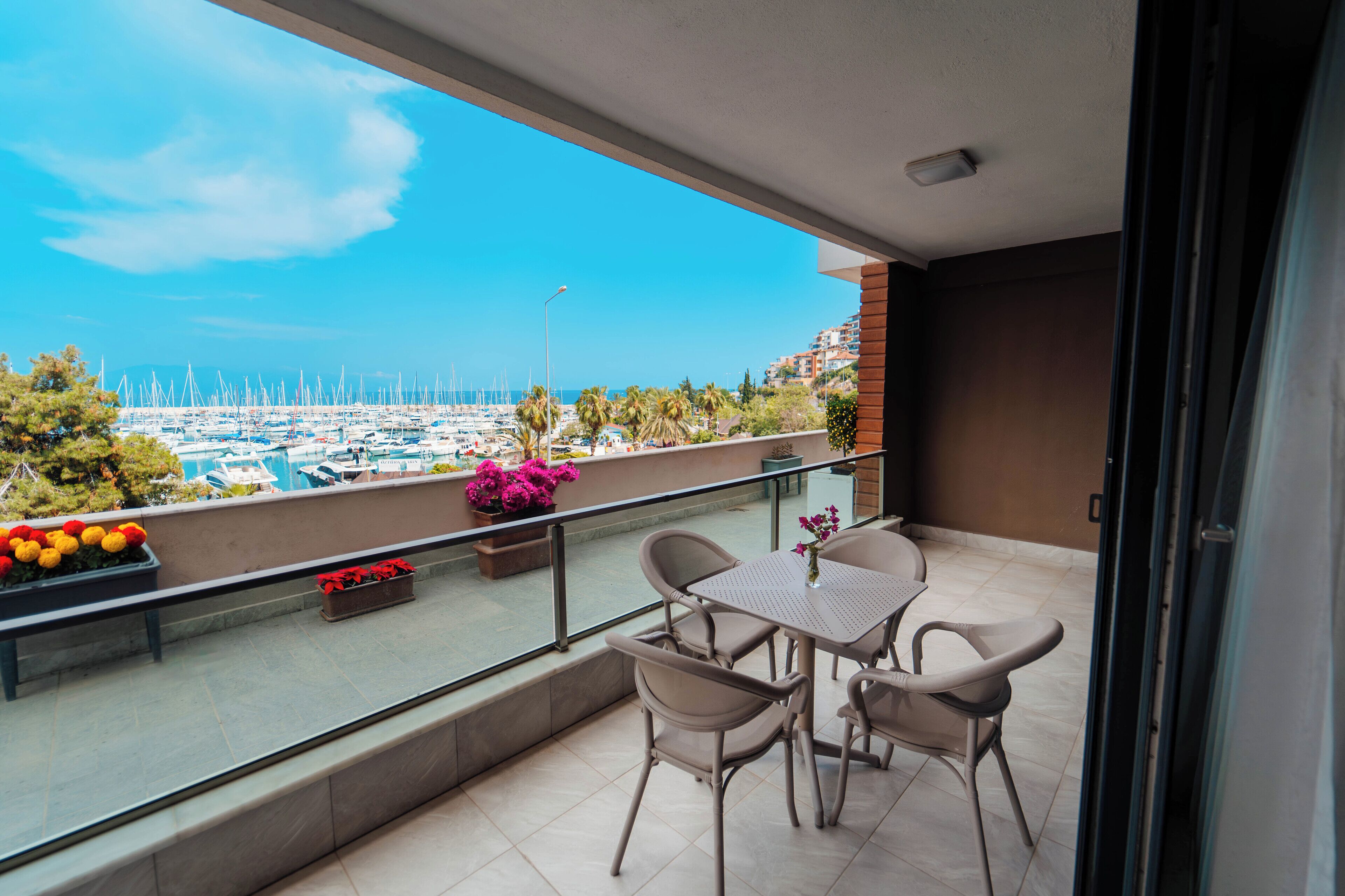 Un balcón con mesa y sillas, con vista a un puerto deportivo con barcos y palmeras.