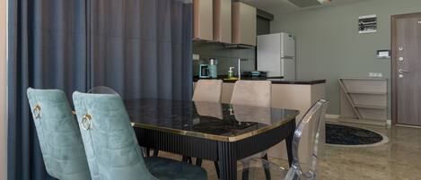 Un comedor moderno con una mesa de vidrio, dos sillas tapizadas, una cocina al fondo y una puerta a la derecha.