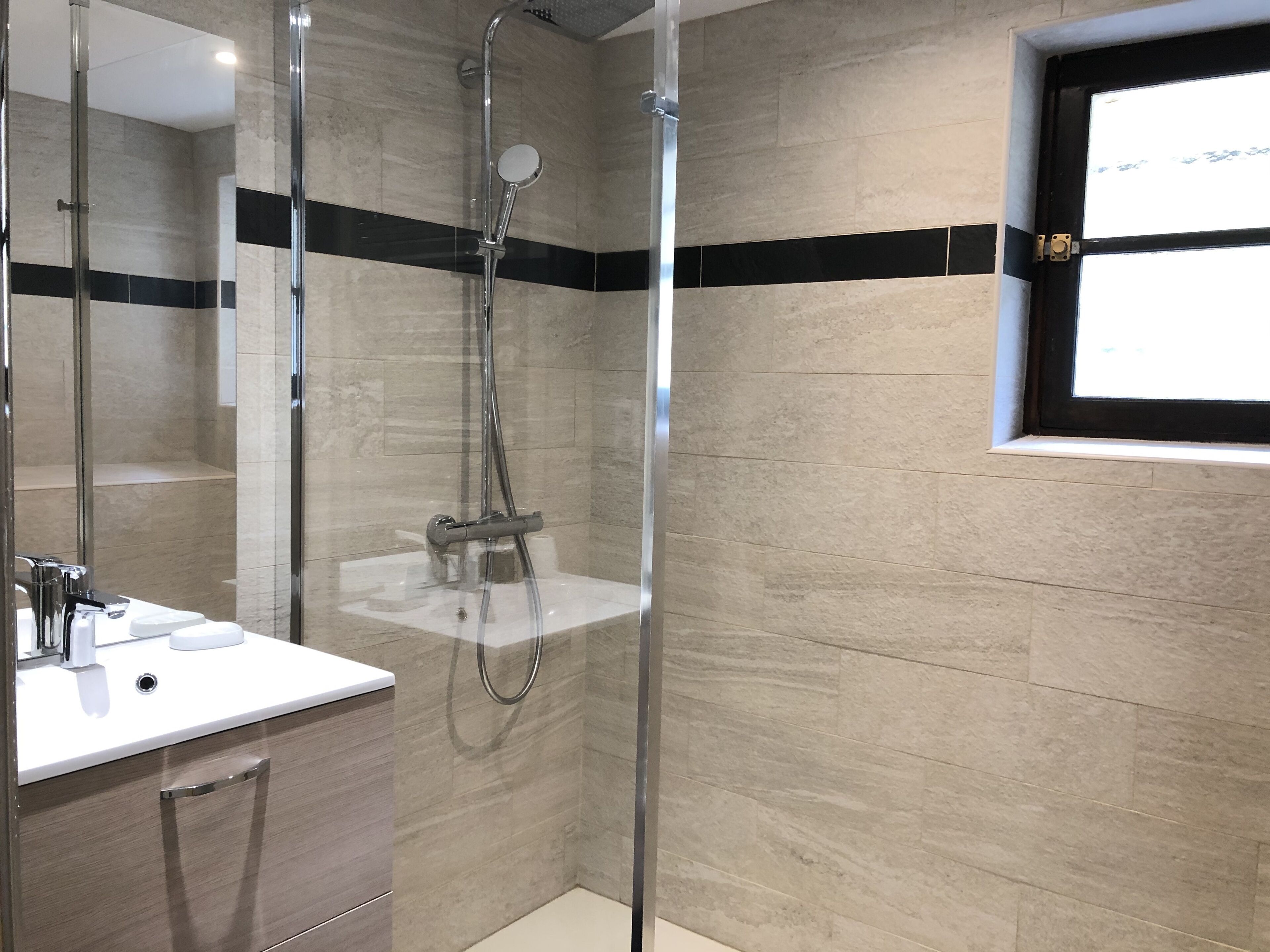 Un baño moderno con ducha envuelta en vidrio, un lavabo blanco y un espejo.