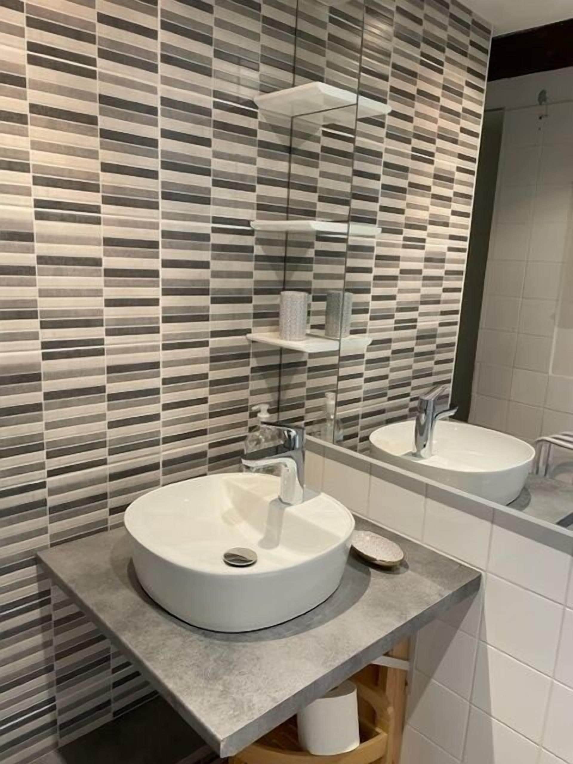 A modern bathroom with a large mirror, two sinks, and a striped tile backsplash.