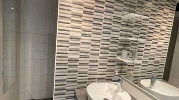 A modern bathroom with a large mirror, two sinks, and a shower.