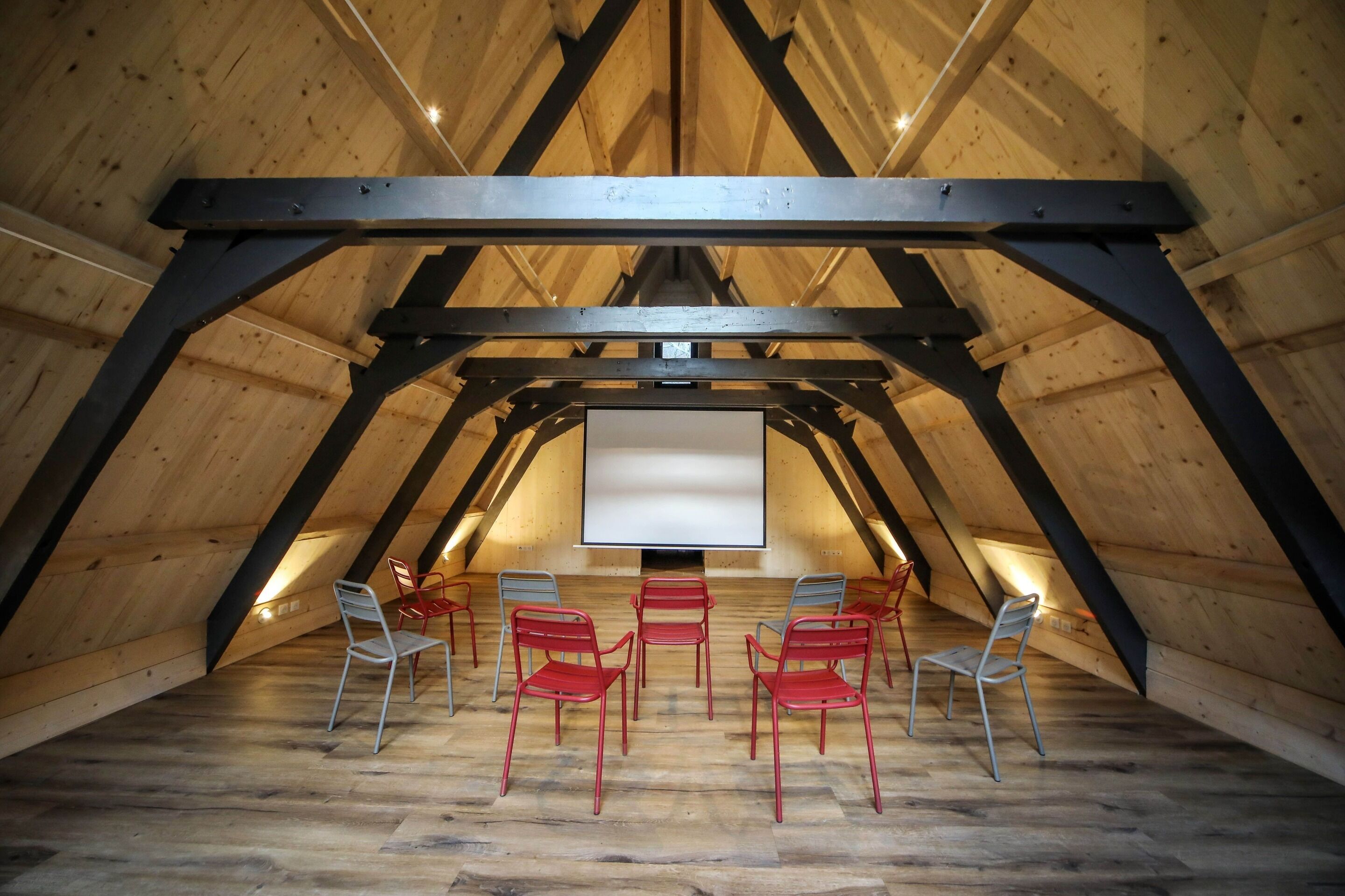 An attic room with a sloped wooden ceiling, a projector screen, and several chairs arranged for viewing.
