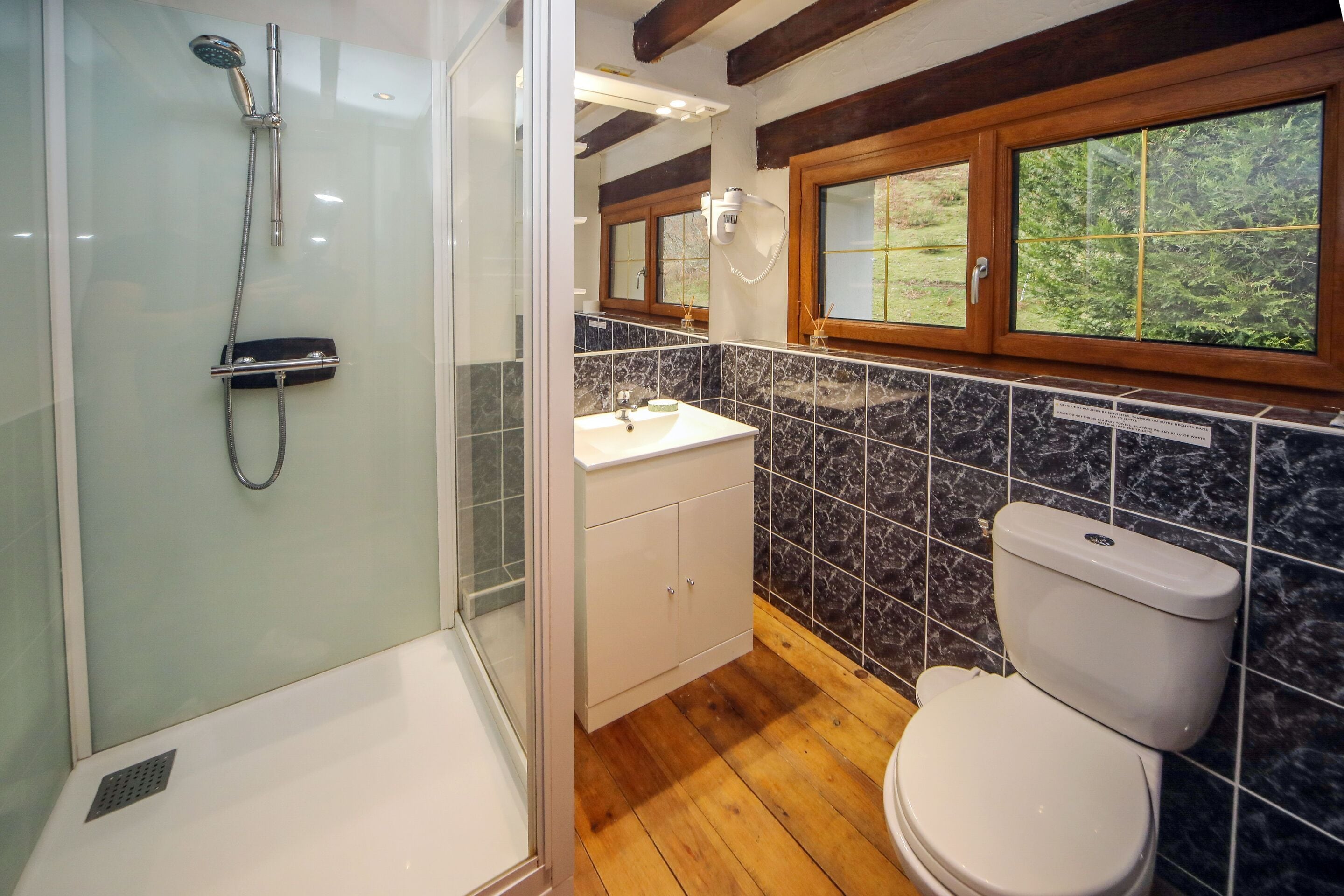 Een badkamer met een douche met glazen wand, houten vloeren, een wit toilet en een wand betegeld met marmer.