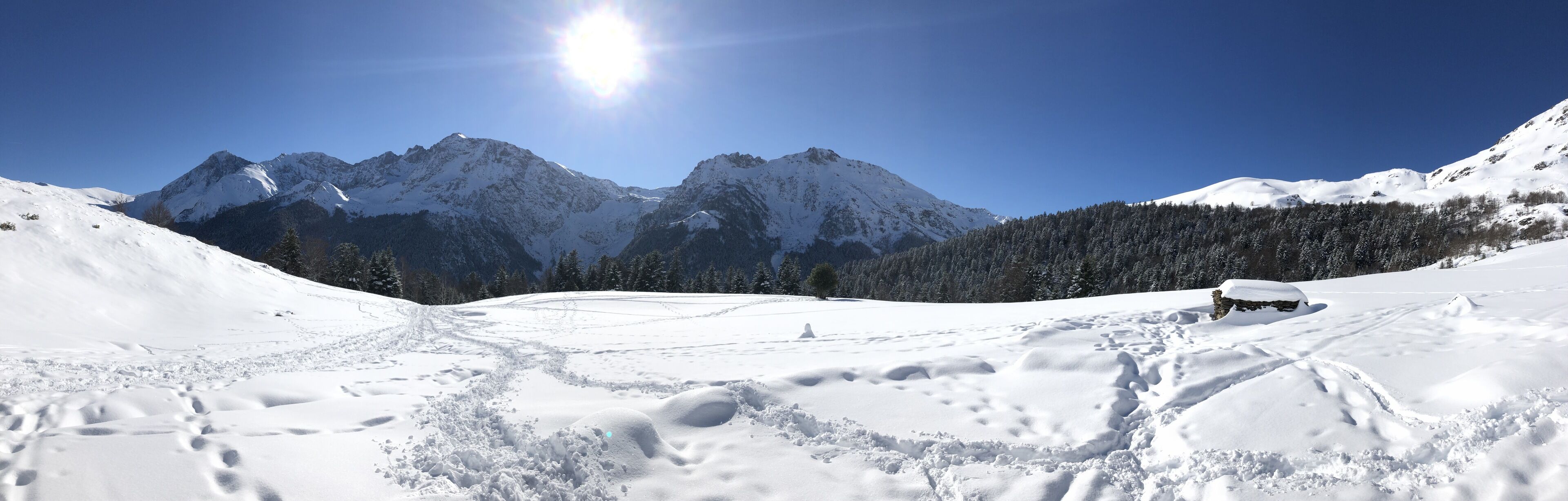 A snowy mountain landscape with clear skies and a bright sun.