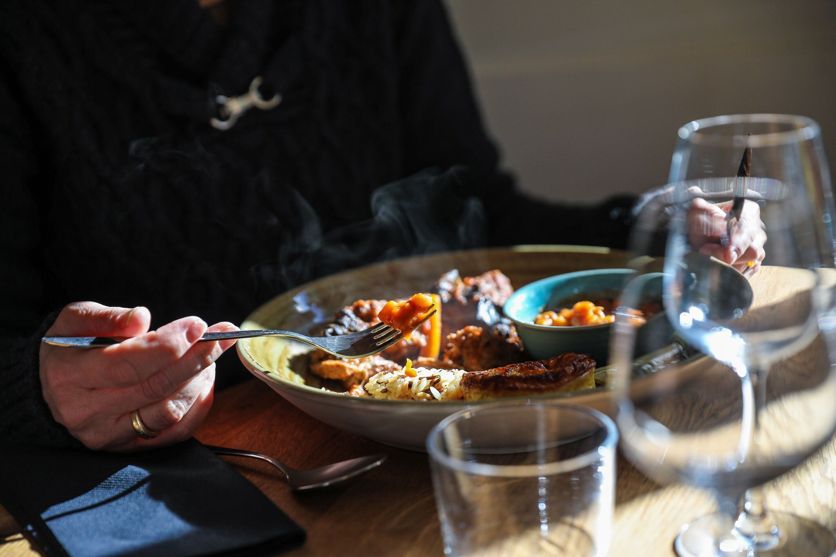 A person dining at a table with a plate of food, a fork, and a glass of water.