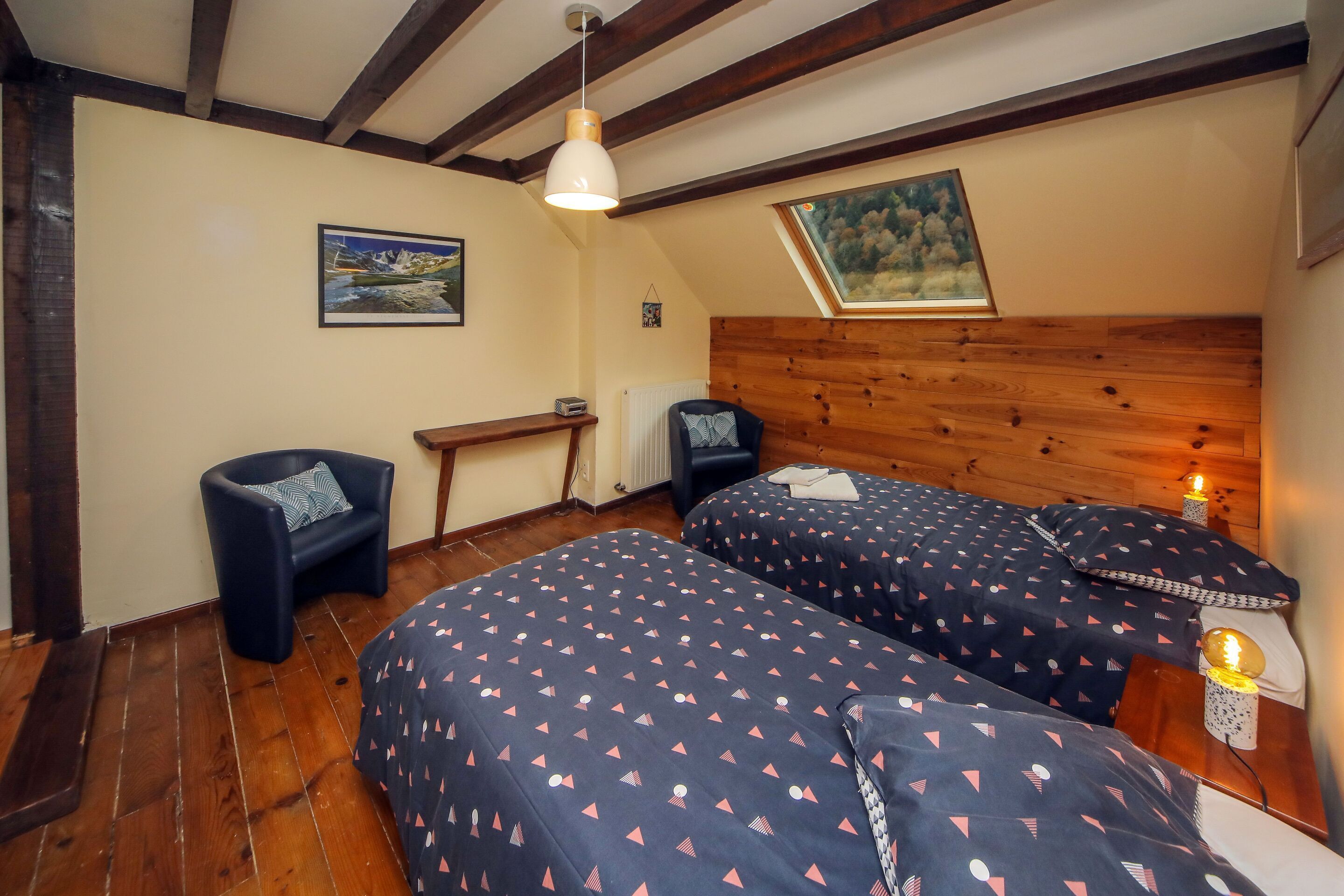 Un dormitorio con dos camas, un cabecero de madera, un escritorio, una silla y una ventana con vistas a montañas.
