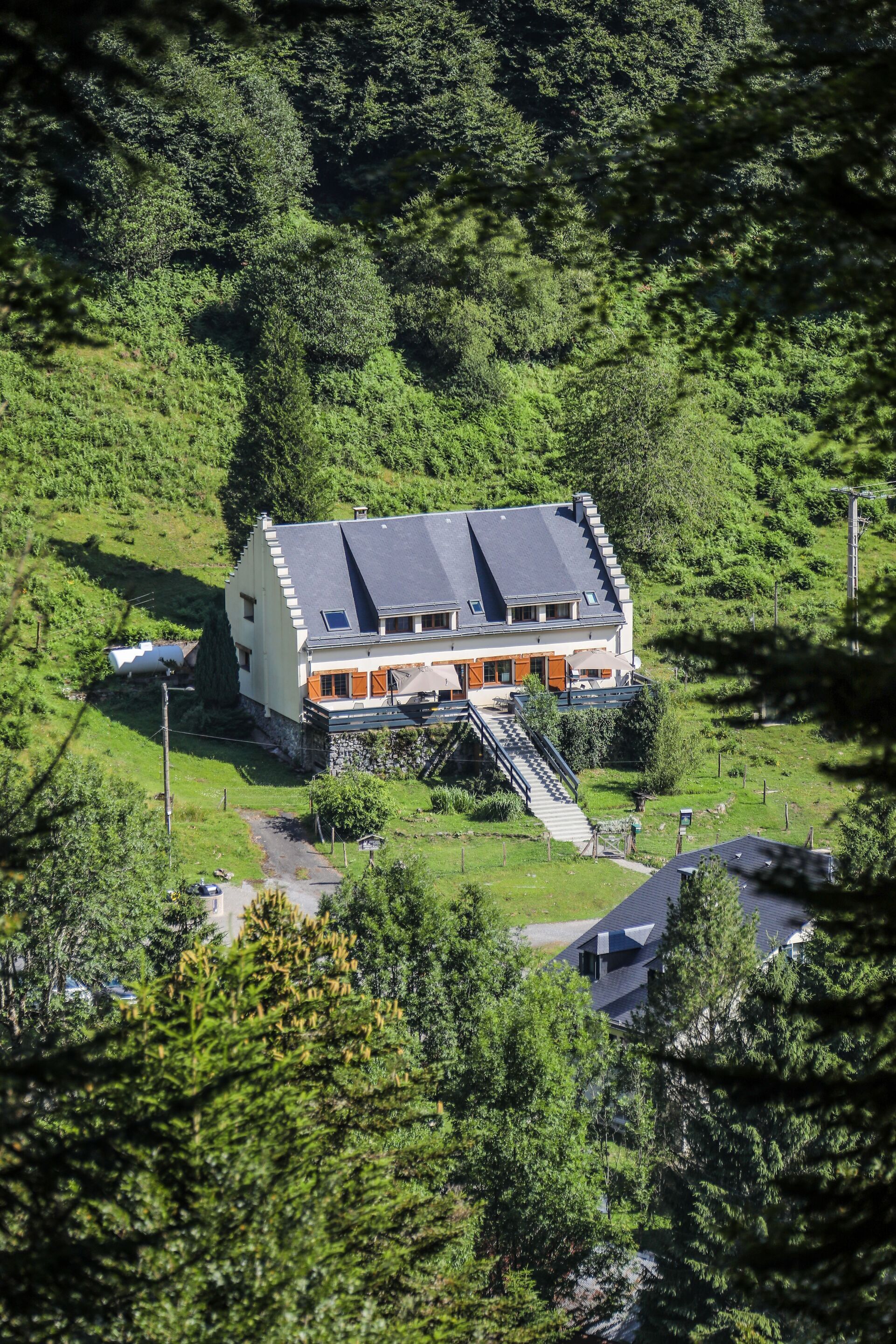 A two-story house with a sloped roof, surrounded by lush greenery.