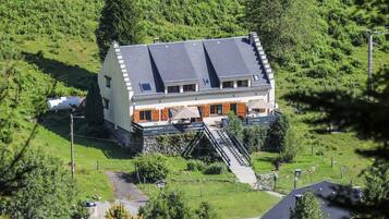 A two-story house with a sloped roof, surrounded by lush greenery.
