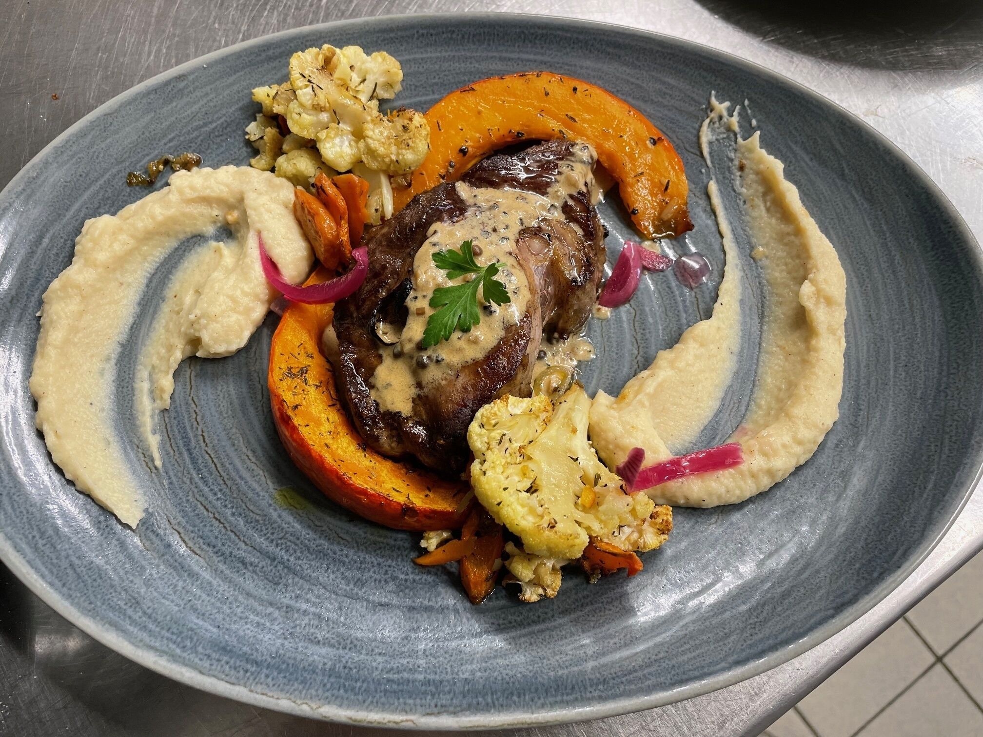 A plate of food with a steak, roasted vegetables, and a creamy sauce.