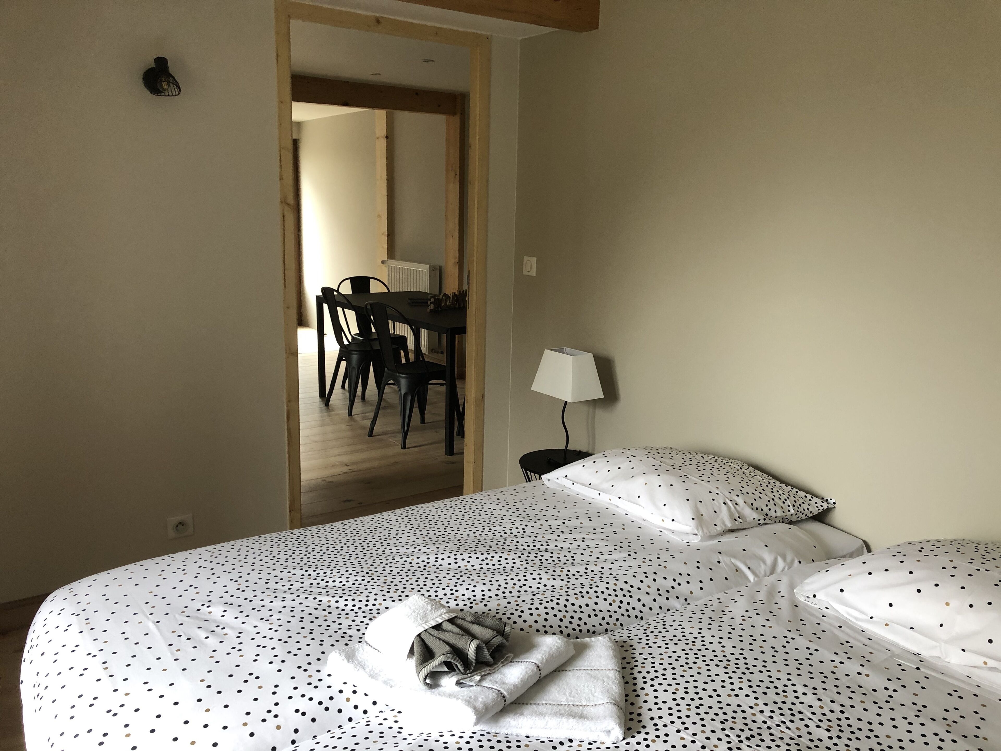 A hotel room with a bed, a nightstand, a lamp, and a view of the dining area.