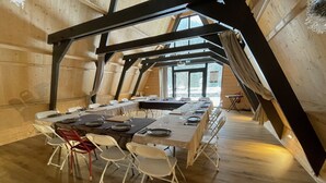 Comedor con una larga mesa dispuesta para seis personas, sillas blancas y una estructura de techo de madera.
