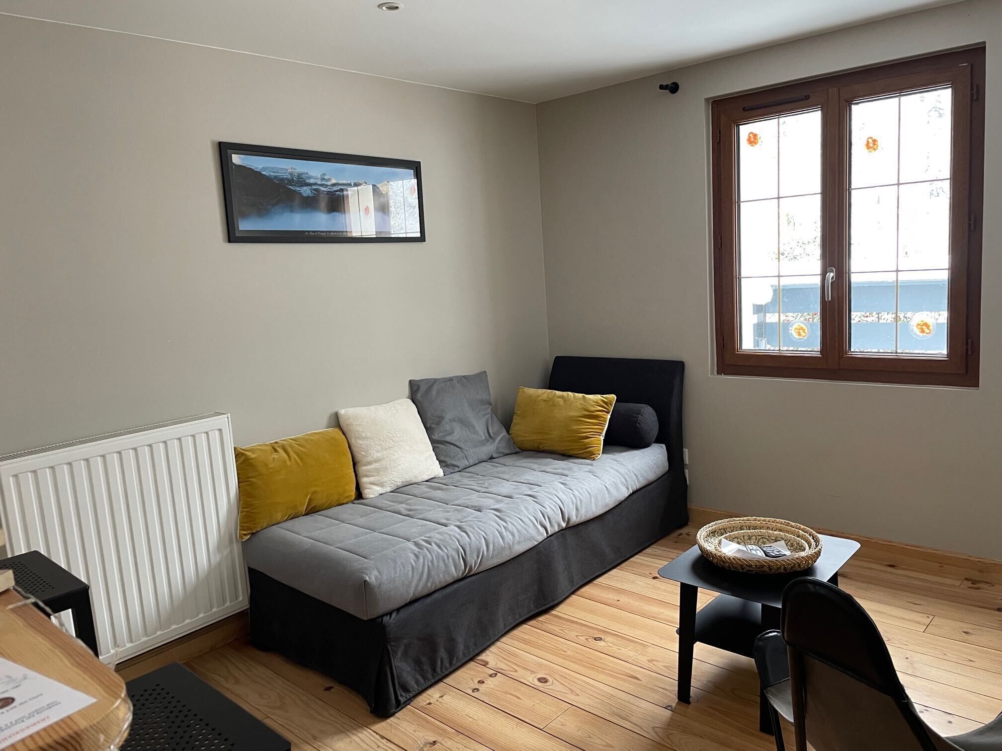 Ein kleiner, gemütlicher Raum mit Bett, Fenster mit Blick, Heizkörper und Tisch mit Korb.