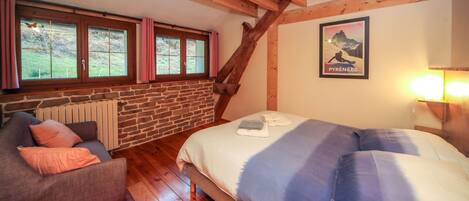 A bedroom with a bed, a sofa, a window with curtains, a wooden ceiling, and a poster on the wall.