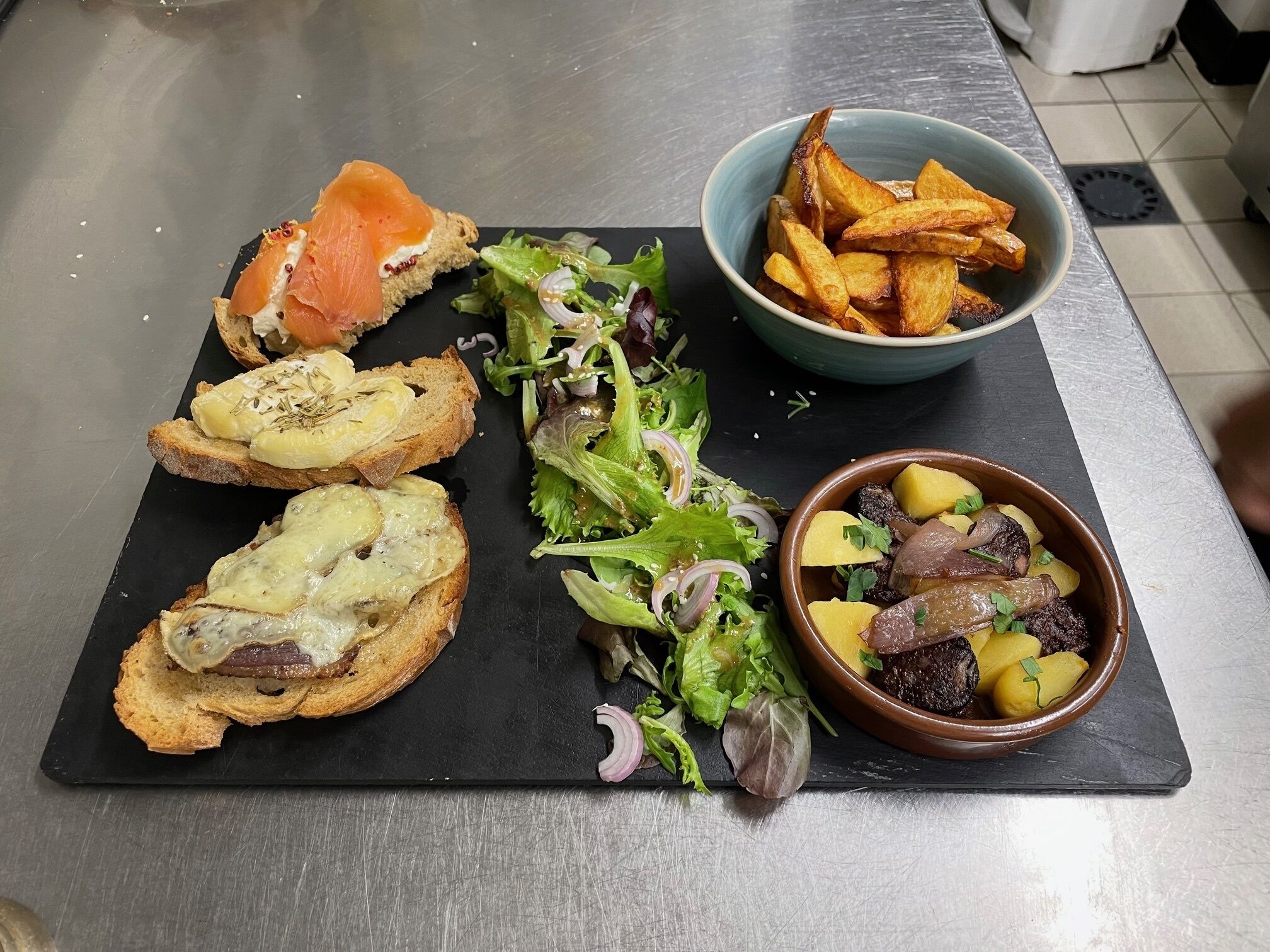 A meal with smoked salmon, roasted potatoes, and a salad on a black slate board.