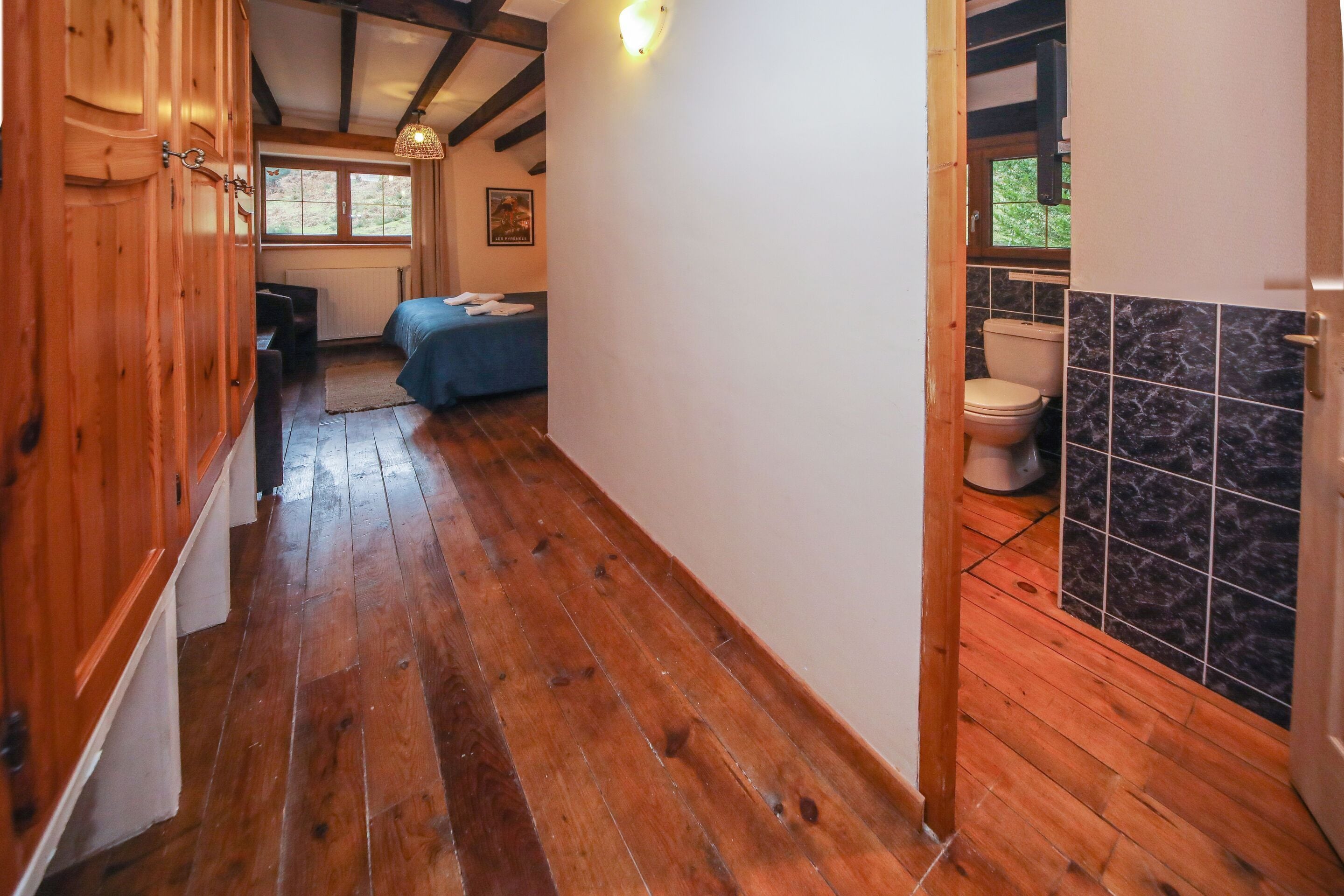 Un estrecho pasillo con suelo de madera que conduce a un dormitorio con cama y un baño con inodoro y paredes con azulejos.
