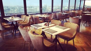 A modern dining area with high tables and cushioned chairs, large windows offering a city view.