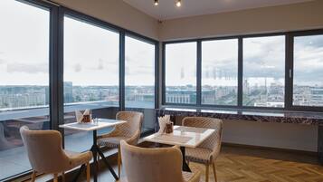 A modern dining area with large windows, wooden flooring, and a city view.