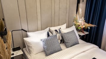 A neatly made bed with white and patterned pillows, a bedside table with a vase of flowers, and a wall-mounted lamp.