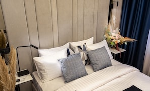 A neatly made bed with white and patterned pillows, a bedside table with a vase of flowers, and a wall-mounted lamp.