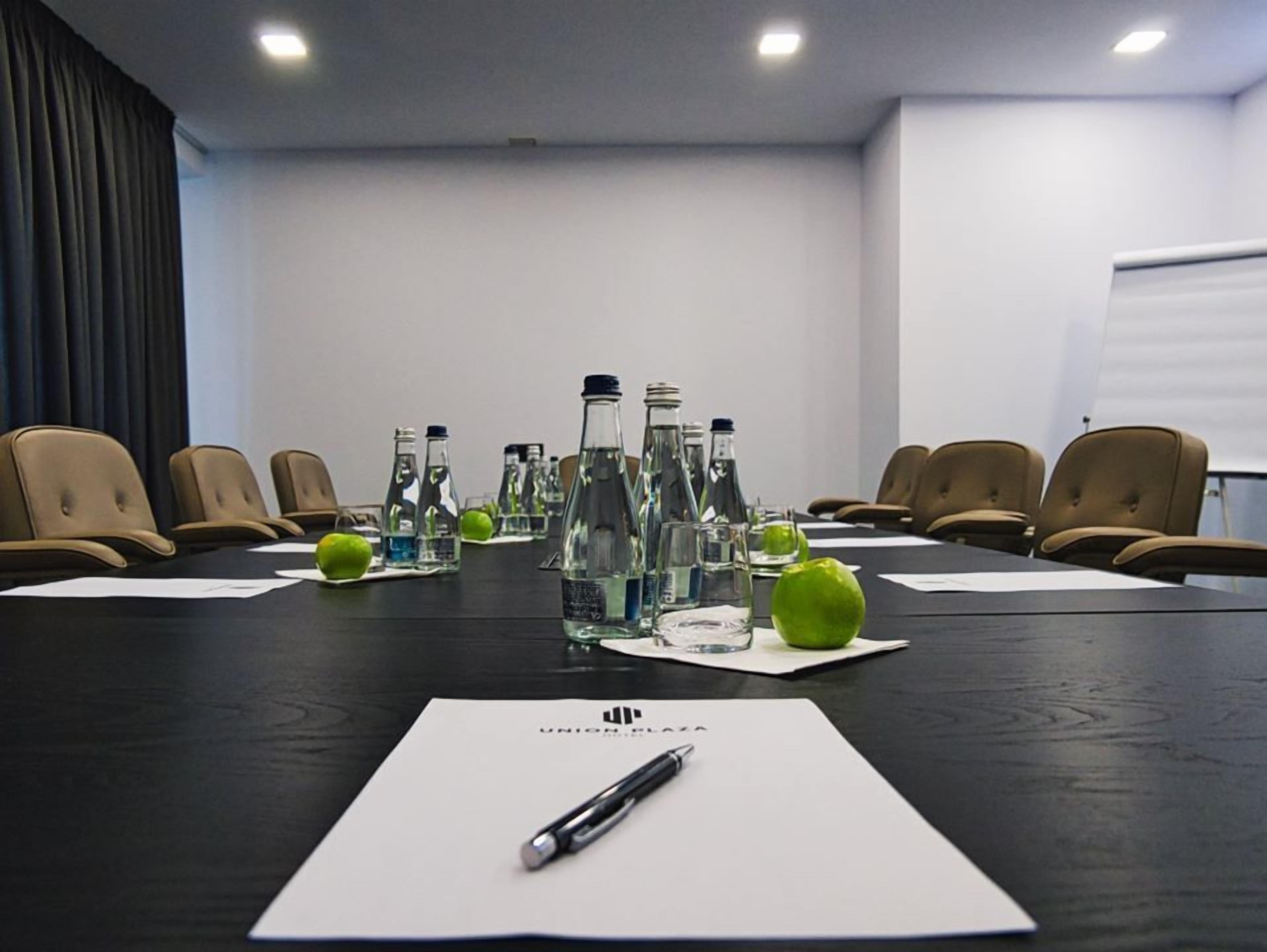 A conference room with a long table, chairs, water bottles, and apples.