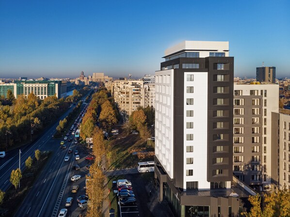A modern building with a flat roof and large windows, surrounded by a busy road and trees.