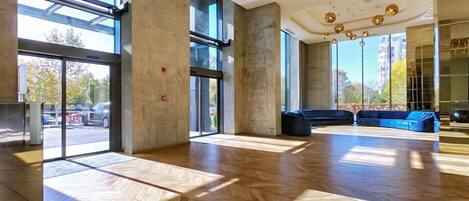 A spacious lobby with large windows, a herringbone wood floor, a blue sofa, and a modern chandelier.