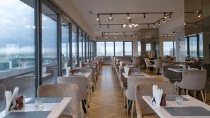 Un restaurante moderno con techos altos, ventanas amplias y vistas a la ciudad.