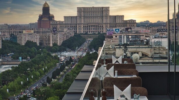 Un paisaje urbano con un edificio destacado de cúpula, una calle concurrida y vistas a un restaurante con terraza.