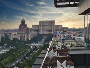 A cityscape with a prominent building with a dome, a busy street, and a view of a restaurant with outdoor seating. - Union Plaza Hotel (Bucharest)