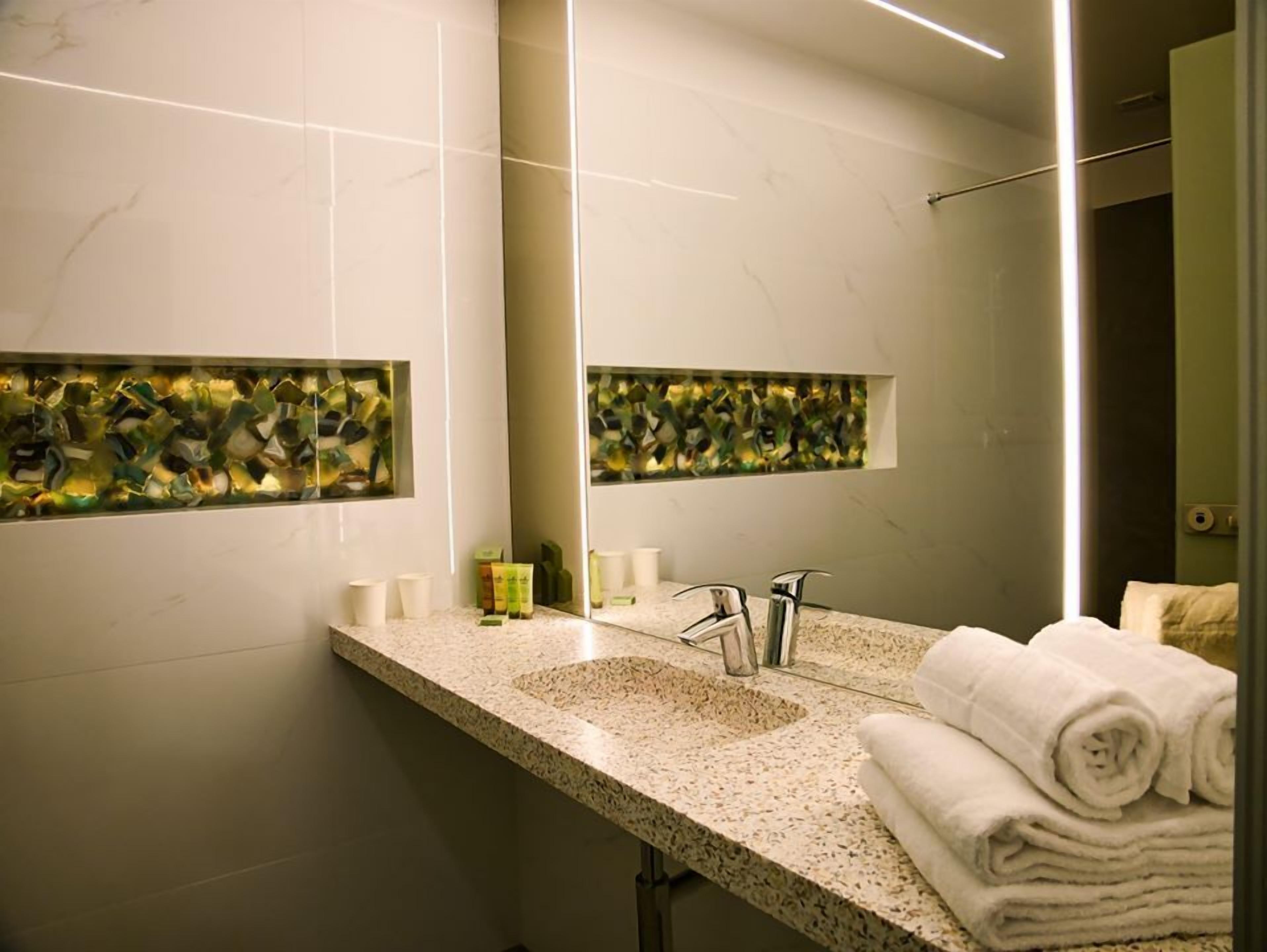 Une salle de bain avec un comptoir en granit, un lavabo, un miroir et un porte-serviettes.