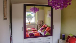 A bedroom with a large wardrobe, a bed with colorful bedding, a window with a view of the outside, and a purple hanging decoration. - Cozy apartment in Rostock with WiFi (Rostock)