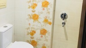 A bathroom with a toilet, a shower with a glass door, and a wall with floral tiles. - Hotel Gaylord (New Delhi)