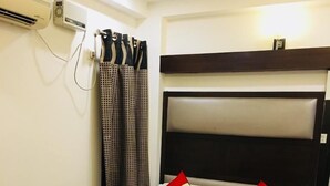 A hotel room with a bed, a nightstand, an air conditioning unit, and curtains. - Hotel Gaylord (New Delhi)