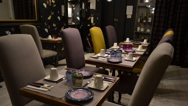 Un comedor con mesas dispuestas para dos, con sillas modernas y una variedad de vajilla.