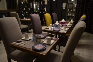 A dining area with tables set for two, featuring modern chairs and a variety of tableware.