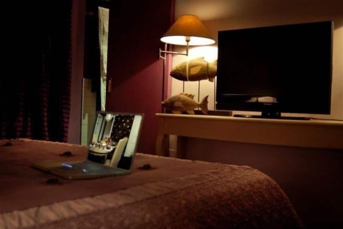 A hotel room with a bed, a desk with a lamp, a television, and a laptop.