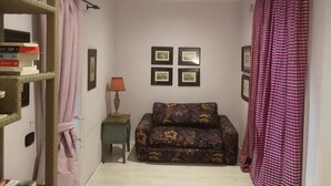 Una sala de estar con un sofá, una mesita de noche con una lámpara, una estantería y una pared decorada con cuadros.
