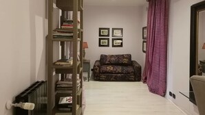 Un estrecho pasillo con una estantería de madera, un sofá estampado y cuadros en la pared.