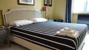 Una cama bien hecha con ropa de cama a rayas, una lámpara de noche y una toalla doblada sobre la cama.