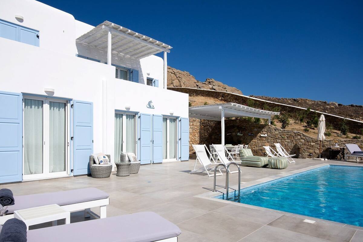 Ein Poolbereich mit Liegestühlen, einem Pool und einem Gebäude mit blauen Türen und Fenstern.
